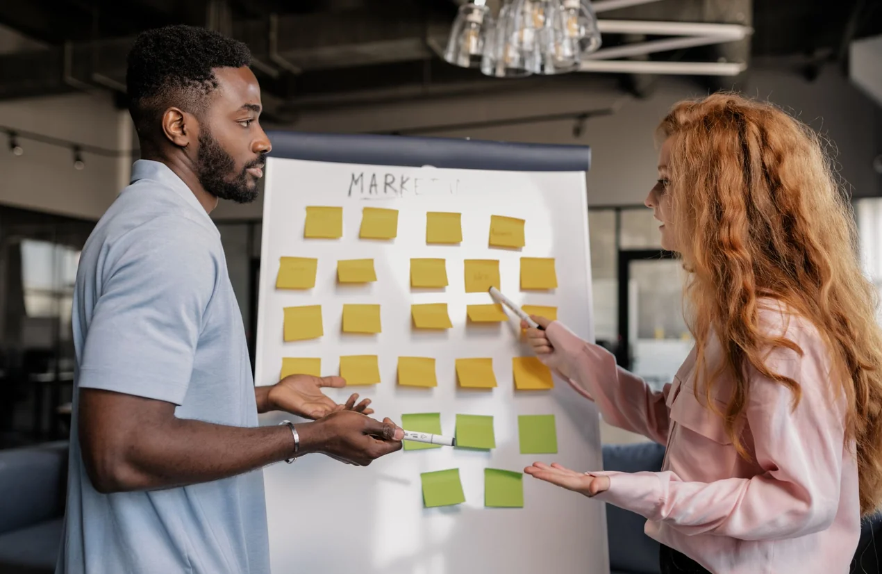 Due persone che organizzano idee con dei post-it su un pannello di marketing